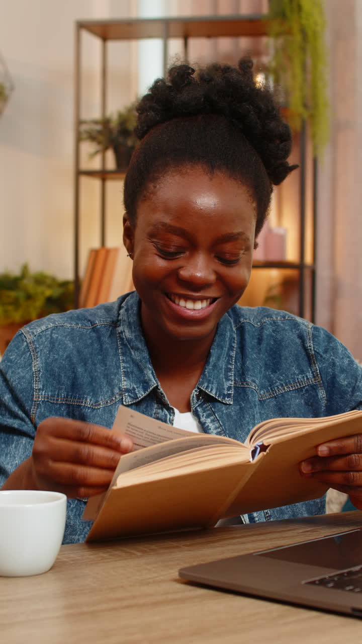 African american young woman reading exciting book with concentration while sitting at table at home