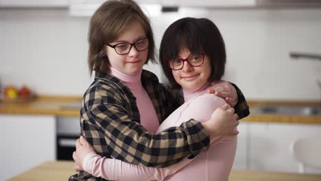 two happy girls with down syndrome in eyeglasses standing together embracing