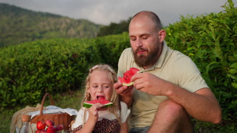 father and daughter enjoying watermelon picnic in a tea plantation