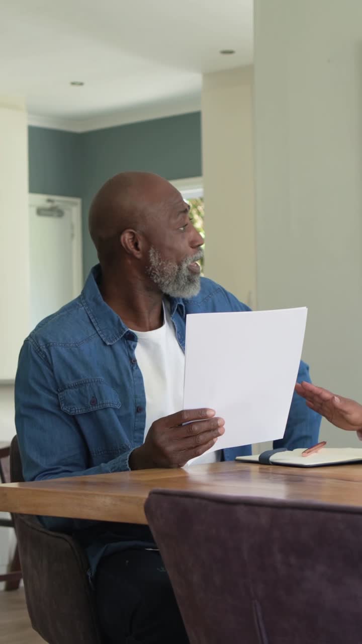 Vertical video: Reading paper, man in denim shirt celebrating and high-fiving partner in kitchen