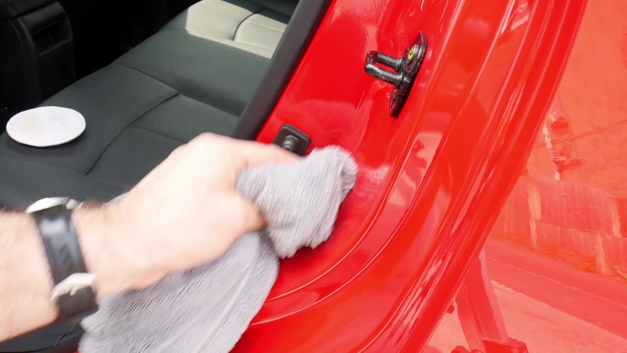 Close up removing polish from a door shut jamb on a red car with a grey microfibre towel