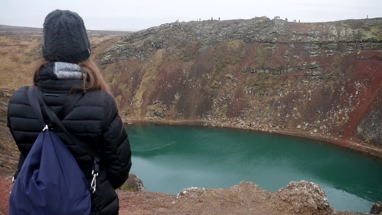 toma cinematográfica de una mujer admirando el lago del cráter kerid en islandia