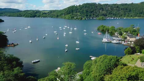 colourful aerial drone view over boats and yachts on lake windermere at bowness marina with hills and trees on a sunny summer morning with blue sky and clouds