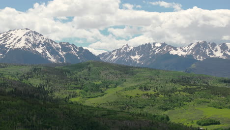 Closeup-aerial-view-of-beautiful-Colorado-mountain-range-with-snow-capped-peaks-on-a-sunny,-blue-sky-day-in-the-summer-with-green-fields-and-trees