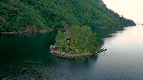 Panoramic-Aerial-of-Red-Cabin-at-Sunrise-on-Small-Island-in-Middle-of-Fjord-Waters,-Lovrafjorden,-Norway