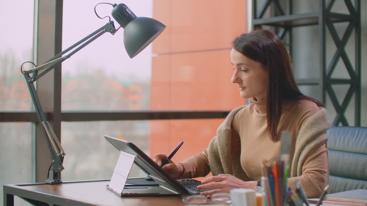 un diseñador profesional en la oficina dibuja con un lápiz en una tableta gráfica sentado en una oficina con grandes ventanas en el estilo loft. oficina moderna de diseñador gráfico y creador.