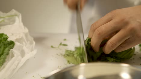 Close-up-of-a-chef-finely-chopping-fresh-herbs-on-a-white-cutting-board,-panning-shot