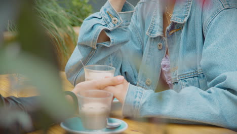 close up of happy same sex female couple meeting and sitting outdoors at coffee shop together