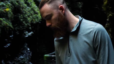 Young-man-slowly-walking-in-cave-like-place-and-looking-down-with-water-trickling