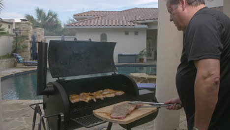 man puts rack of bbq ribs on to hot grill in his back yard