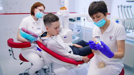 child in dental chair. doctor dentist showing plastic model jaws to little boy