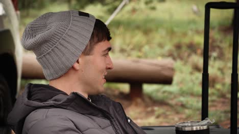 man sitting at campsite outdoors talks in slow motions and smiles