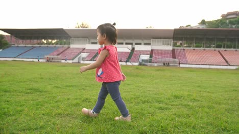 asian little girl walking on the grass at stadium