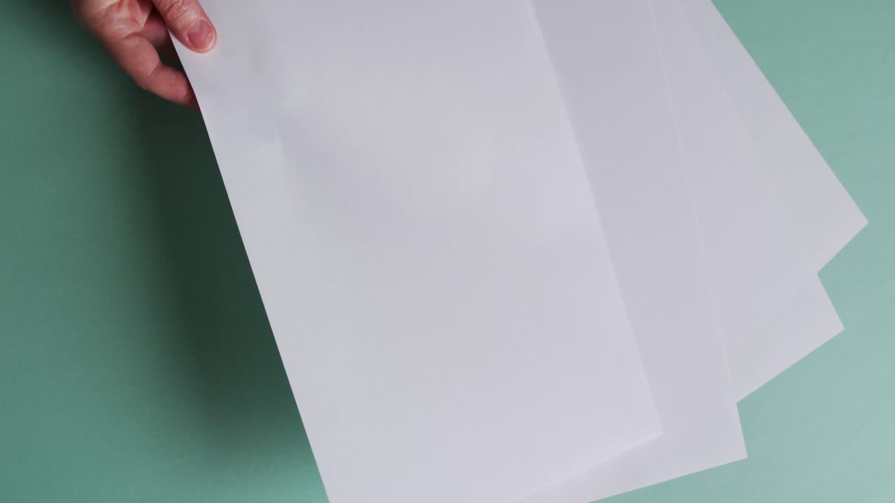 mano sosteniendo un pedazo de papel sobre pedazos de papel con espacio de copia en fondo verde en cámara lenta