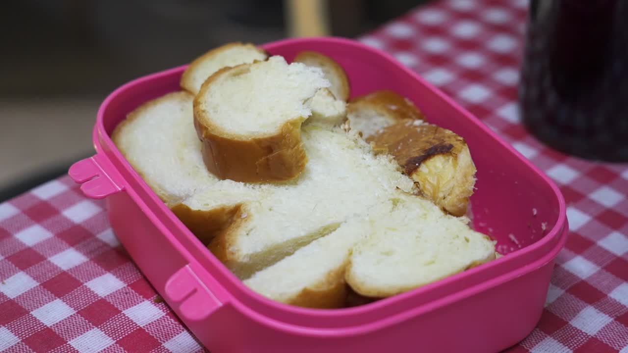 Slices of white bread in a pink plastic container on a checkered tablecloth