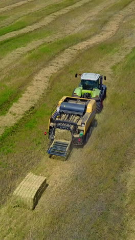 tractor collects dry hay. aerial flight view of a cube baler tractor discharges a fresh wheat bale during harvesting vertical video