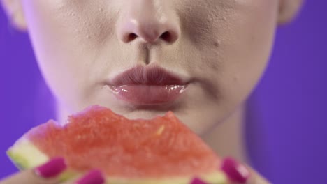 close up of woman's mouth taking a bite and eating watermelon fruit, studio shot with purple background