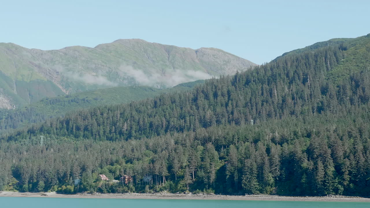 Dolly shot from the water of Mountains in the Alaska Countryside near Juneau, showing forests in the distance and trees along the coastline.