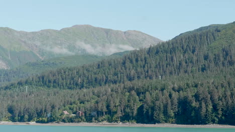 dolly shot from the water of mountains in the alaska countryside near juneau, showing forests in the distance and trees along the coastline.