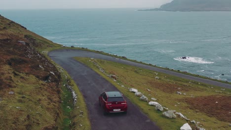 aerial view of red car moving on beautiful curved coastal road. ireland, achill island