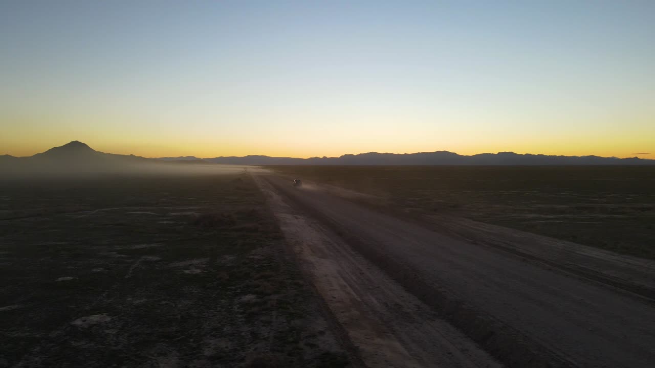 Truck driving down a dusty desert off-road trail at dusk - aerial view