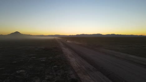truck driving down a dusty desert off-road trail at dusk - aerial view