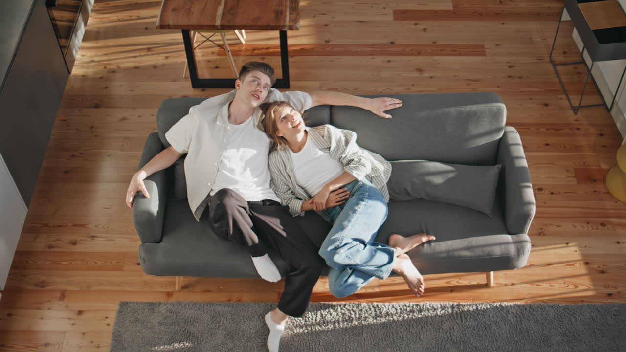 Affectionate sweethearts cuddling home in sunlight. Top view happy couple talk