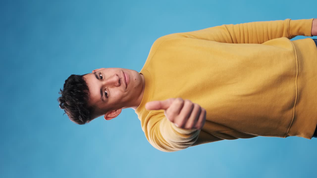 Young man with thumb up to show agreement or approval while standing on an isolated background.
