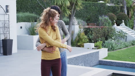 happy caucasian lesbian couple dancing, embracing and smiling in front of house