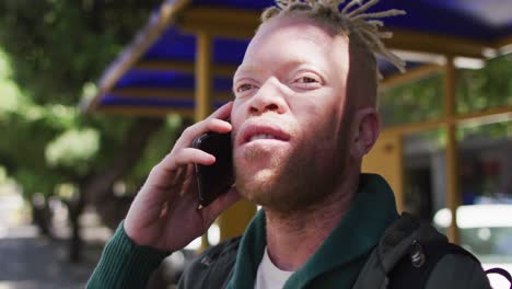 Happy-albino-african-american-man-with-dreadlocks-in-park-talking-on-smartphone