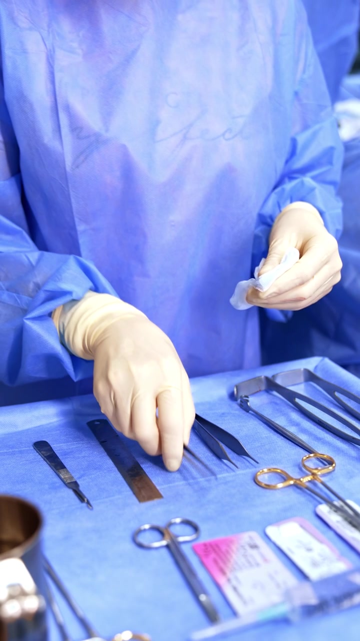 Unrecognized medic wearing blue rope and white latex gloves cleans metal tools at the surgical stand. Scrub nurse assisting in the surgery room during the operation. Vertical video.