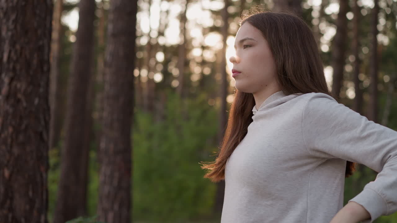 여자 운동 선수는 숲에서 뒷 해가 지는 동안 팔을 따뜻하게합니다. 밀집된 나무들 사이에서 경로를 따라 조하기 전에 심장 운동. 신선한 공기에서 집중적인 운동.