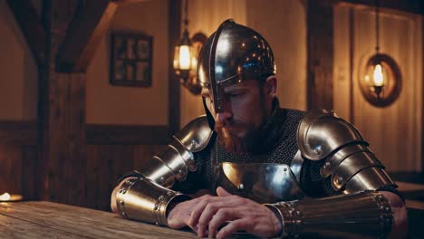 medieval knight wearing full steel armor and chainmail, sitting pensively at wooden table inside dimly lit tavern, waiting for hearty meal with serious, anticipatory expression