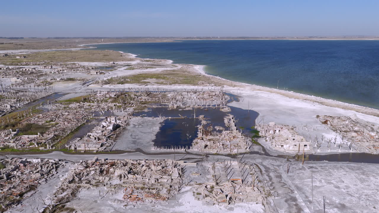 Drone vista over Villa Epecuén’s salt-covered ruins and shore, showing geometric blocks and blue lake at the site of Argentina’s iconic flooded spa town