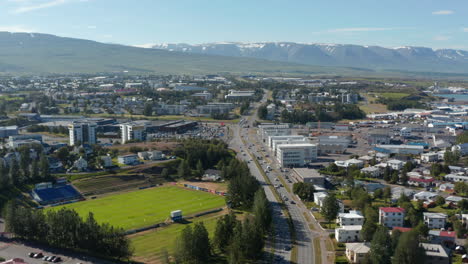 Imágenes-Aéreas-De-Una-Carretera-De-Varios-Carriles-Que-Atraviesa-El-Barrio-Urbano.-Montañas-Cubiertas-De-Nieve-En-El-Fondo.-Akureyri,-Islandia