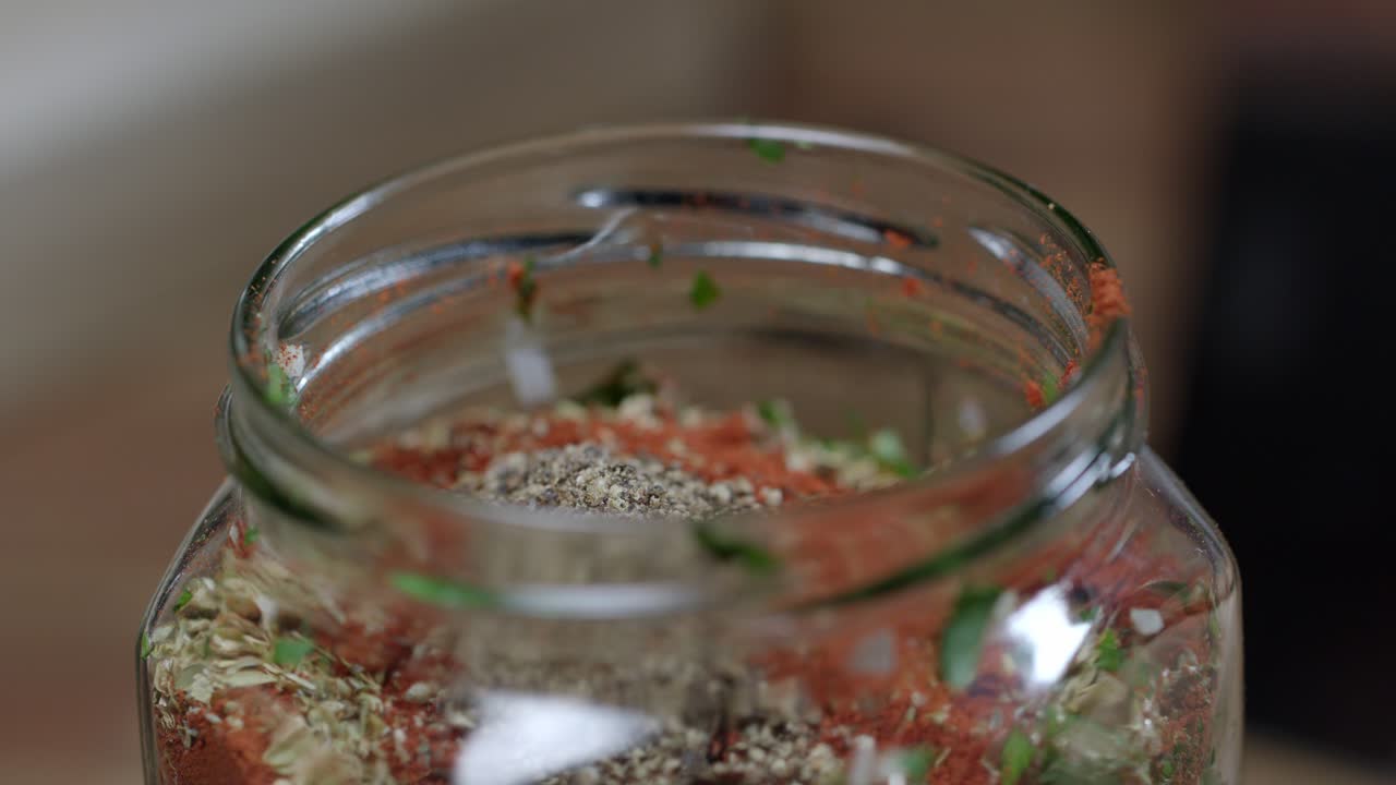 Adding spices with a spoon to the chimichurri sauce in the glass container where it is preserved
