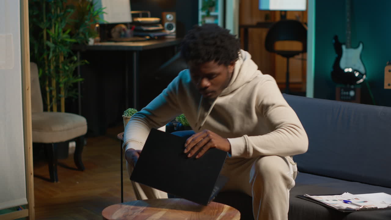 Ambitious black man learning a new language alone in his cozy living room, browsing internet for study platforms and explanations. Adult using language learning software online on laptop. Camera A.