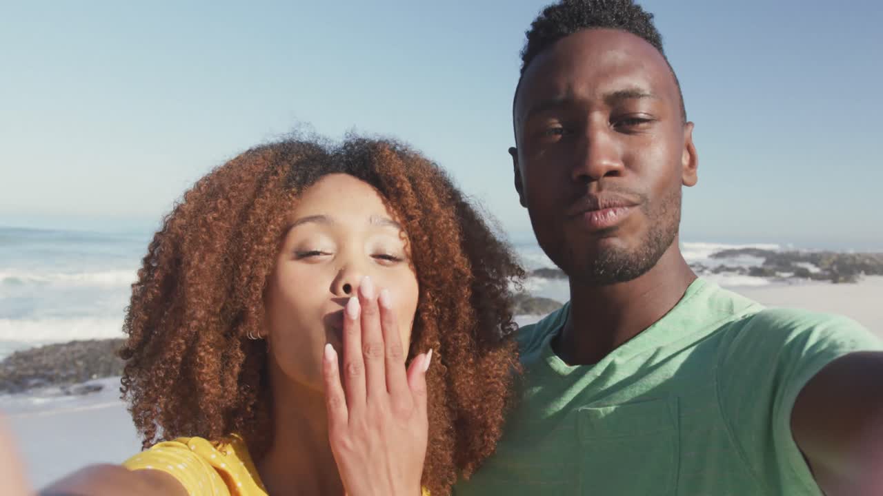 pareja afroamericana enviando besos a través de la cámara frente al mar