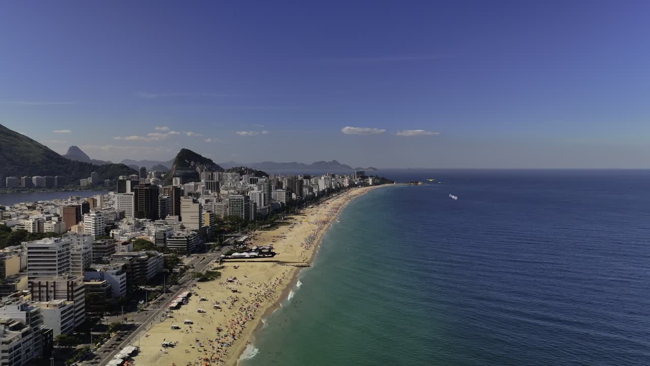 Aerial view of Leblon Beach in Rio de Janeiro with vibrant cityscape along the coastline and deep blue ocean. Establishing drone aerial view