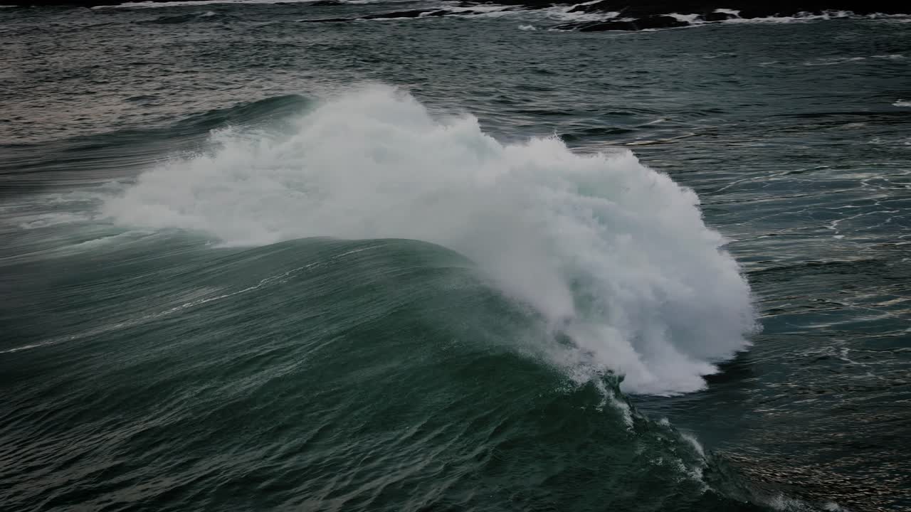 Slow motion tracking of large ocean wave curling and breaking with dramatic energy and sea spray, mist rising off top
