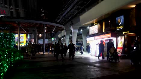 pan from right to left outside yurakucho station at night with commuters and tourists walking by.  pan stops at an izakaya-japanese restaurant with tables outside.
