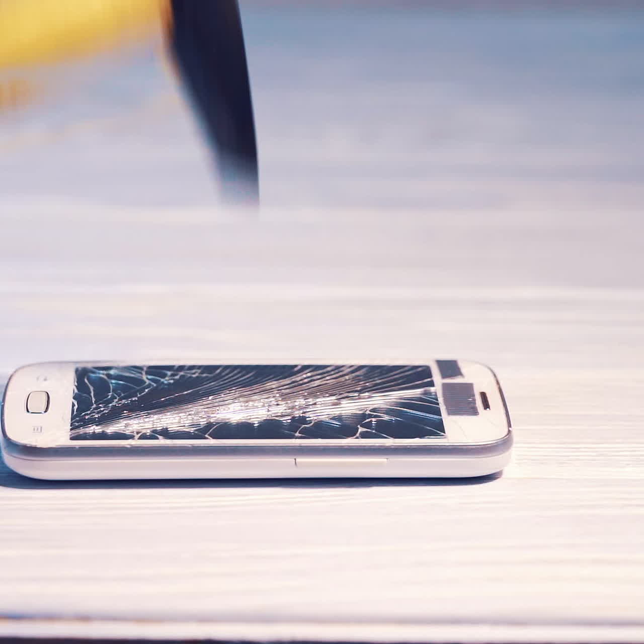 Destruction of a cell phone with a hammer. Smartphone screen cracked by hammer on floor background. Phone screen is broken