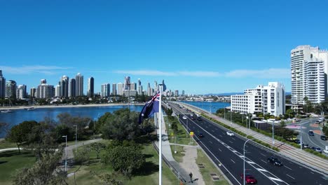 australian flag waving in a strong breeze next to a busy road network leading into a towering city skyline