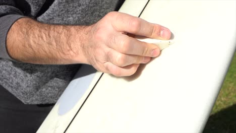 detail of a surfer's hand putting wax on the board