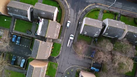 top-down view of a residential area in edinburgh, featuring buildings, parking lots, and roadways. cars are visible on streets and driveways, with green spaces and trees between housing units.