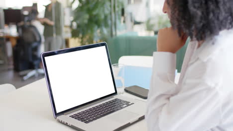 mujer de negocios biracial viendo una computadora portátil con espacio de copia en la pantalla en la oficina, cámara lenta