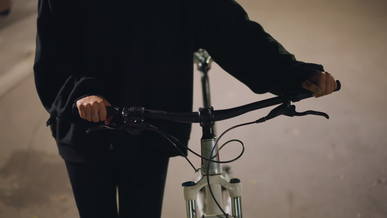 Person In Hoodie Steering Bike Through Tunnel, Close View Of Hands Controlling Bicycle In City Transit, Individual Wearing Dark Hoodie Guiding Bicycle Carefully Through Urban Tunnel Environment