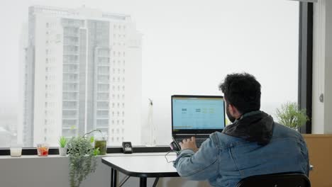man working on laptop with city view from window