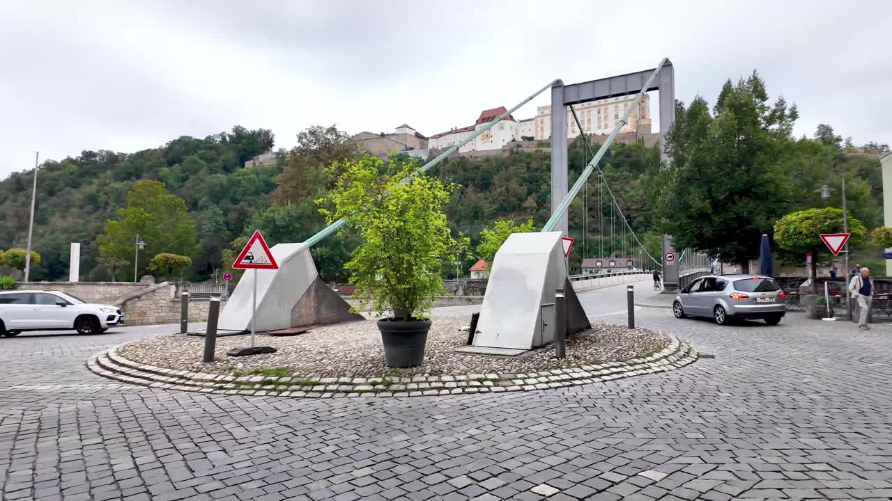 Walking on cobbled street with the view over to pedestrian bridge and castle on the hill, Passau in Germany. Runner, cyclists and cars with a corner restaurant