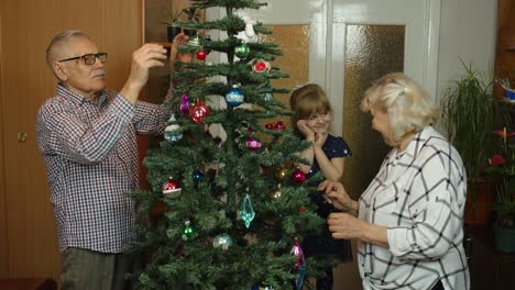 Kleines-Mädchen-Mit-Großmutter-Und-Großvater,-Die-Einen-Künstlichen-Weihnachtsbaum-Mit-Spielzeug-Dekorieren